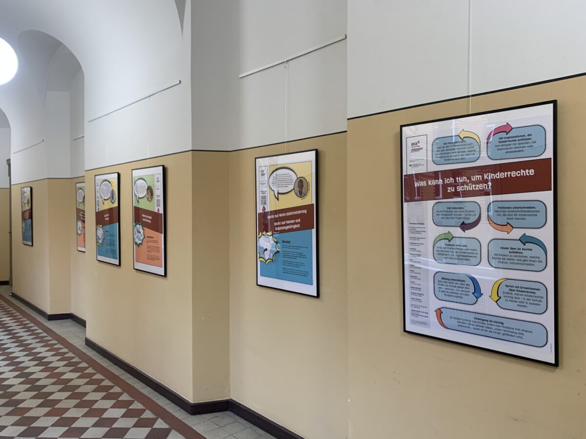 Flur mit Schachbrettboden und mehreren gerahmten Infoplakaten an der Wand, u. a. „Was kann ich tun, um Kinderrechte zu schützen?“